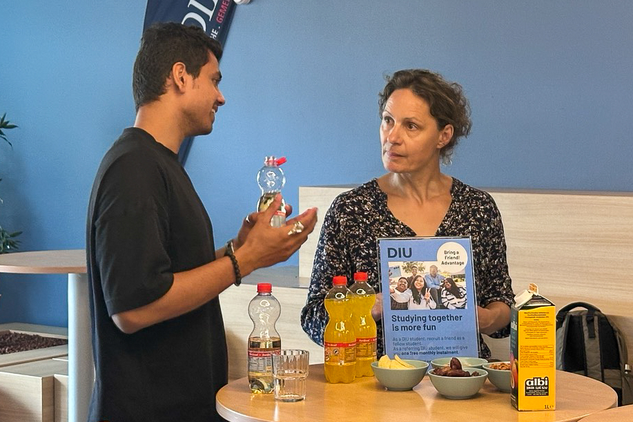 Two people talking at a table with bottles, bowls, and a sign about studying together