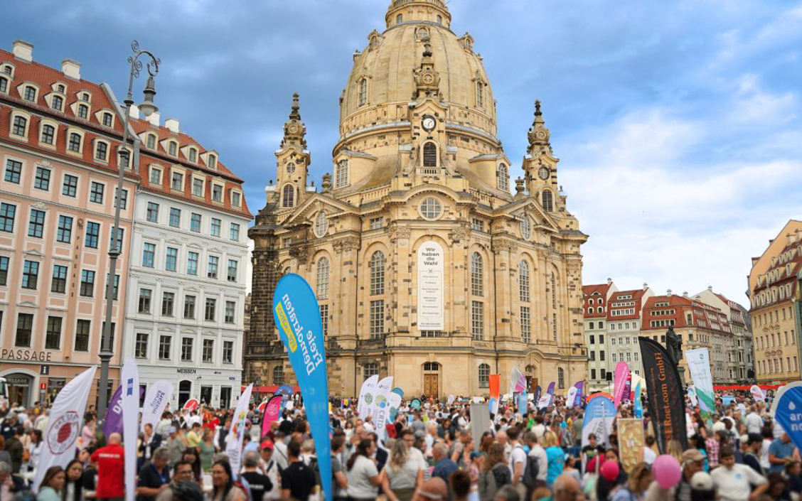 Große Menschenmenge mit bunten Fahnen vor der barocken Frauenkirche in Dresden