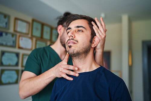 Man sitting with head slightly tilted back while another person examines his cervical spine with hands