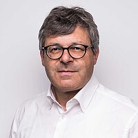 Mann mit grauen Haaren und Brille in weißem Hemd vor hellem Hintergrund