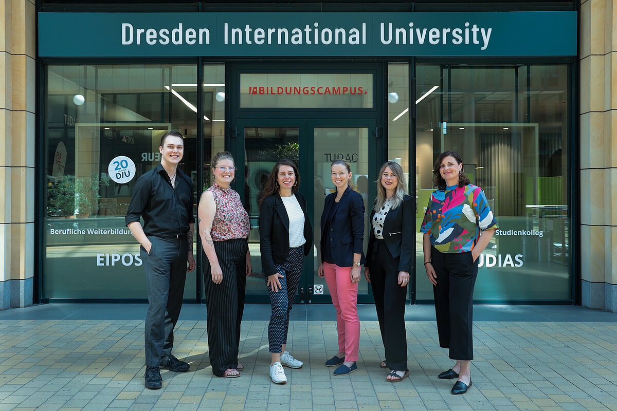 Sechs Personen stehen vor dem Eingang der Dresden International University und blicken in die Kamera