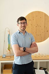 Man with glasses wearing a blue polo shirt standing with arms crossed in front of a model spinep