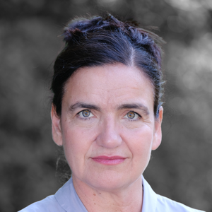 Porträt einer Frau mit dunklen Haaren, die zu einem Dutt gebunden sind, mit hellem Blazer vor unscharfem Hintergrund