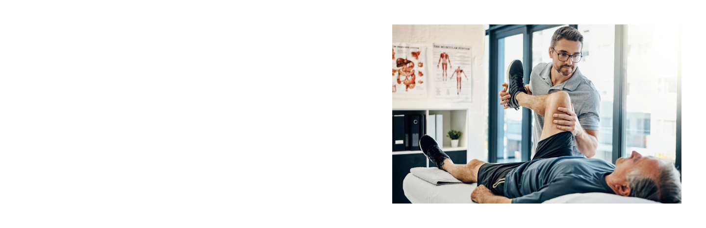 Physiotherapeut mit Brille mobilisiert das Bein eines älteren Patienten auf einer Behandlungsliege in einer hellen physiotherapeutischen Praxis mit anatomischen Wandpostern im Hintergrund.